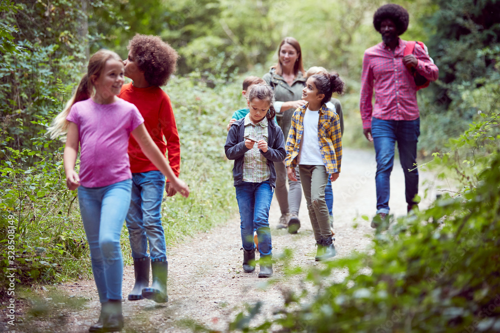 Adult Team Leaders With Group Of Children At Outdoor Activity Camp Walking Through Woodland Adult Team Leaders With Group Of Children At Outdoor Activity Camp Walking Through Woodland