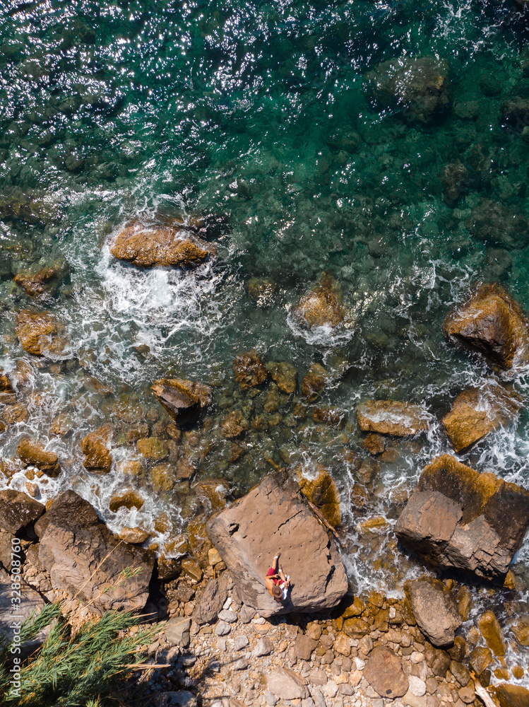Top down aerial view of rocky beach, coastline of the village of Nerano. Wild beach of Italy. vertical photo. Vacation and travel concept. Two people, couple of tourists is sitting on rock. Top down aerial view of rocky beach, coastline of the village of Nerano. Wild beach of Italy. vertical photo. Vacation and travel concept. Two people, couple of tourists is sitting on rock.