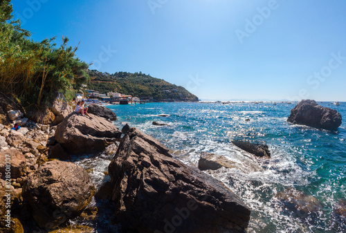 View of paradise, couple of tourists is sitting and look at distace. coastline of the village of Nerano. Wild beach of Italy. Turquoise, blue surface of the water. Vacation and travel concept.