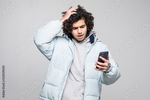 Young curly man holding phone remeber something hold hands on head isolated on white background photo