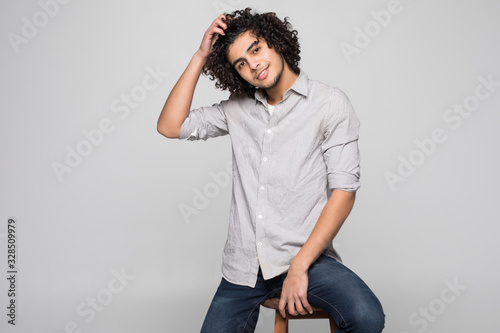 Handsome young man with curly hair sitting on chair over white background photo