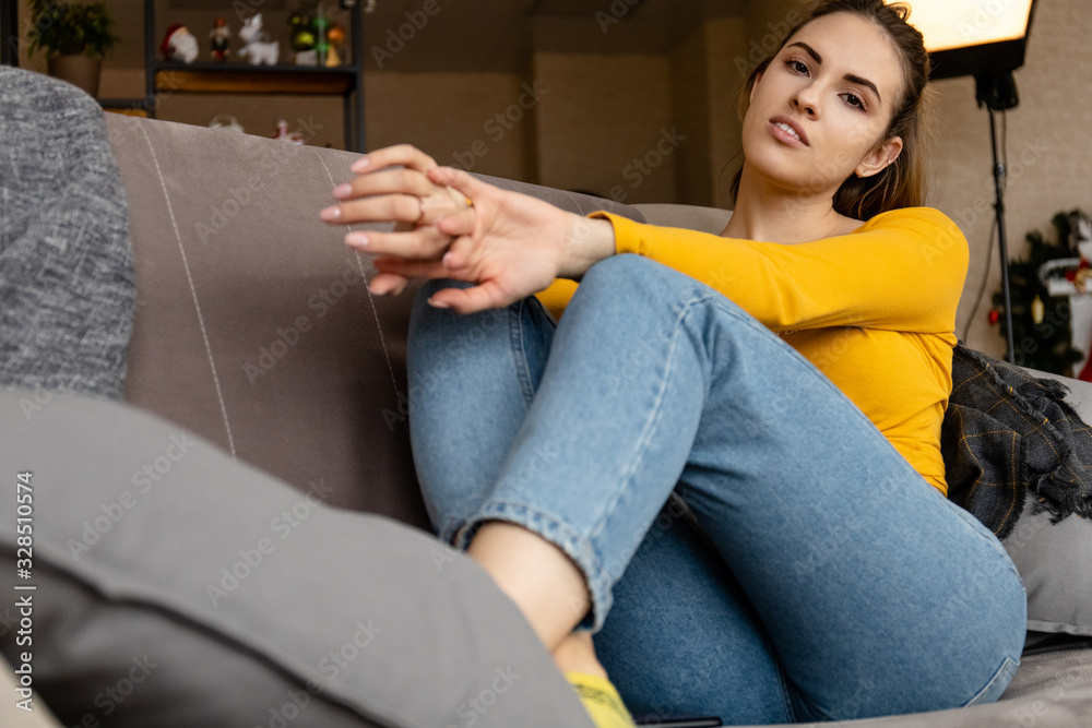 young beautiful girl with a cute face in an orange sweater and jeans is resting while sitting on a sofa young beautiful girl with a cute face in an orange sweater and jeans is resting while sitting on a sofa