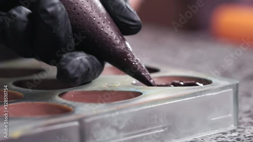 Confectioner filling polycarbonate bonbon mold with creamy chocolate from the piping bag