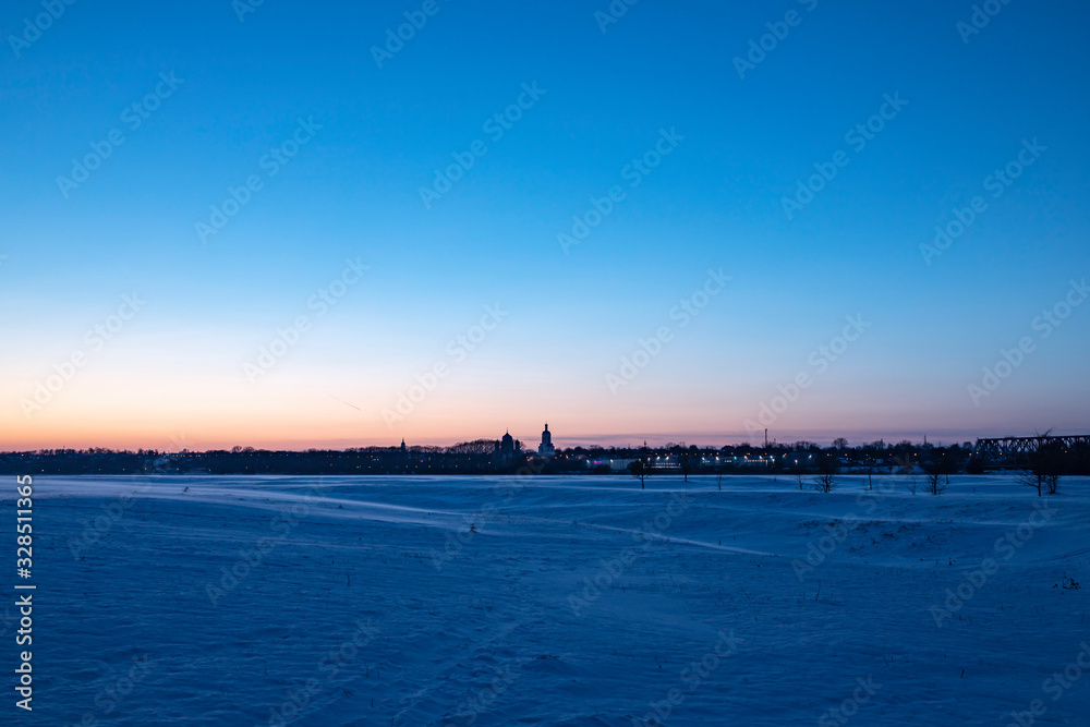 Snowy plain under the sunset sky. Bell tower small town skyline. Snowy plain under the sunset sky. Bell tower small town skyline.