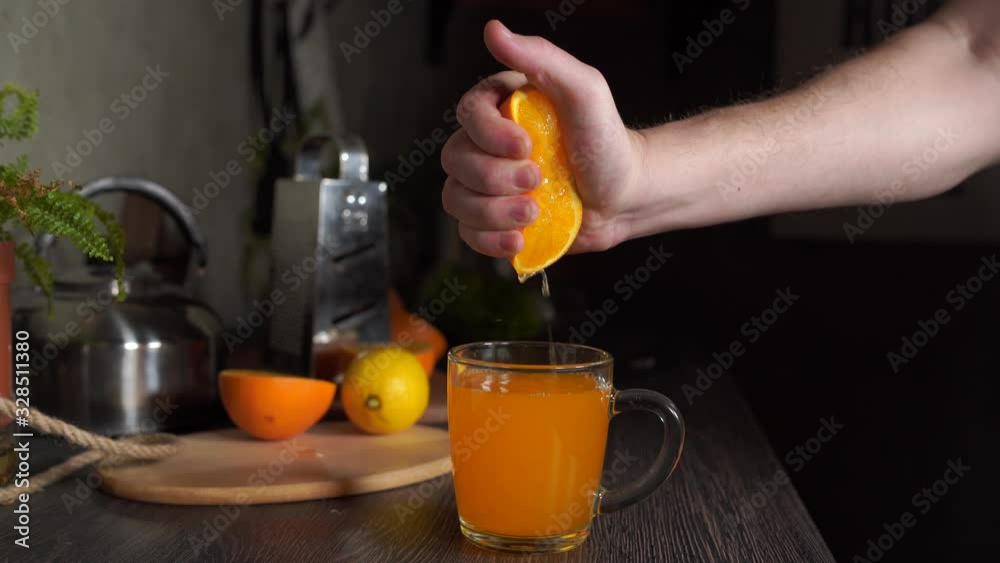 A man squeezes an orange in the kitchen to get freshly squeezed orange juice, close-up. A man squeezes an orange in the kitchen to get freshly squeezed orange juice, close-up.