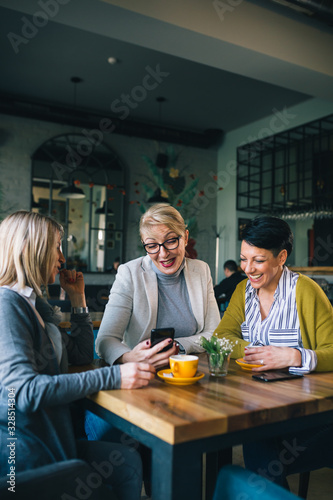 woman friends on coffee break at cafe, using smartphone