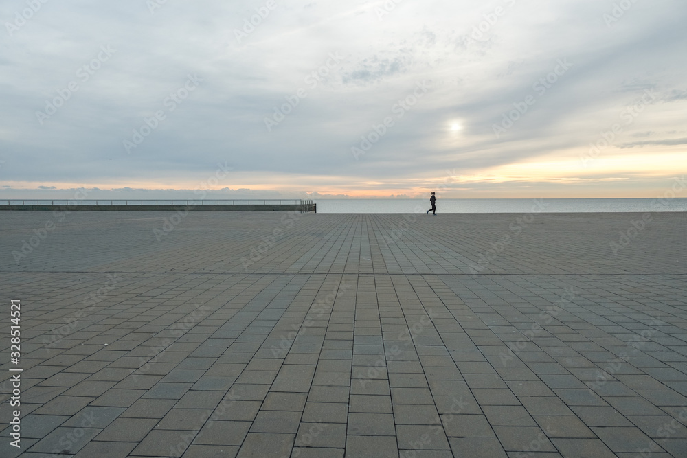 Hombre caminando al amanecer con mar y cielo de fondo. Barcelona, España	