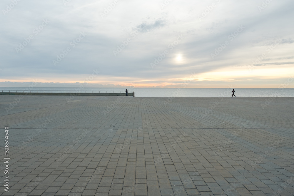 Hombre caminando al amanecer con mar y cielo de fondo. Barcelona, España