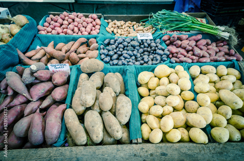 Green garlic bunch and potatoes  sweet potatoes  onion at farmer market stand in Puyallup  WA