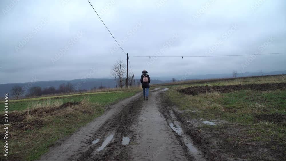 Road in mountains, early spring, rainy weather. Girl walking on dirt road.Wide angle