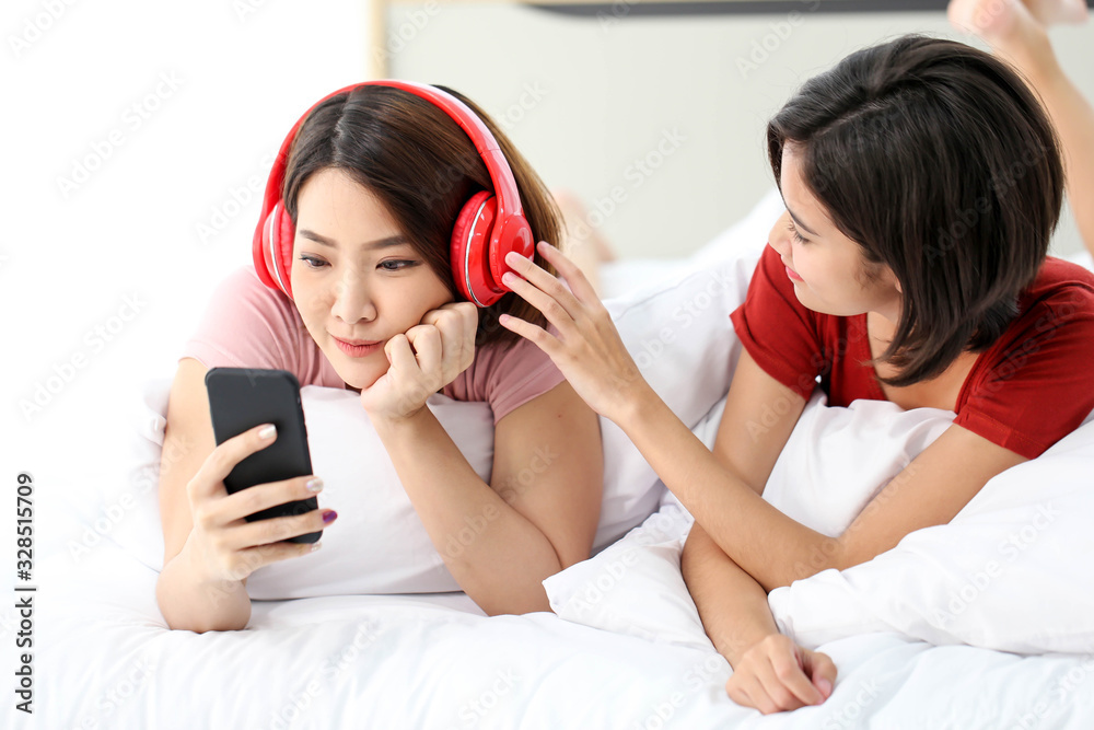 Happy Couple asia woman wear headphones and enjoy musics playing mobile phone and tablet in bedroom. Happy Couple asia woman wear headphones and enjoy musics playing mobile phone and tablet in bedroom.