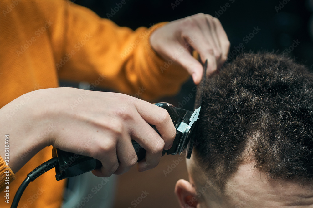 Hairdresser cuts a young man with a hair clipper. Laying curly hair. Professional