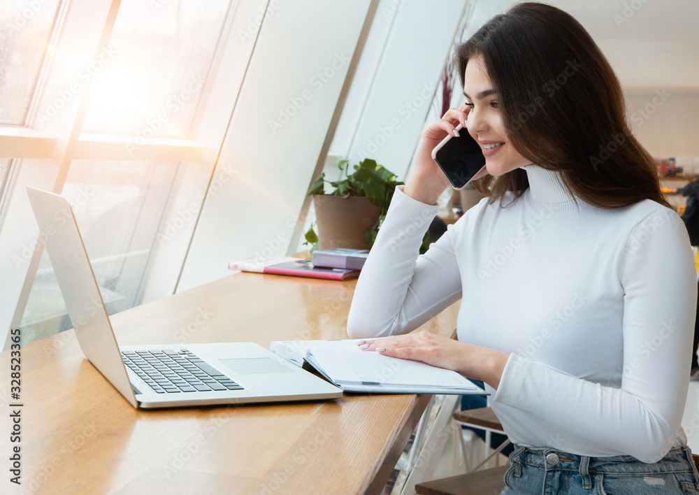 young beautiful businesswoman works in her laptop and speaks on the phone while sitting in the cafe during lunch break, multitasking concept young beautiful businesswoman works in her laptop and speaks on the phone while sitting in the cafe during lunch break, multitasking concept