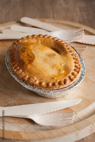 Savoury meat or steak pie in a foil tray with wooden cutlery