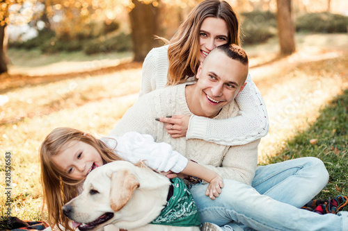 Happy beautiful family with dog labrador is having fun  are sitting on green grass in park. © zadorozhna