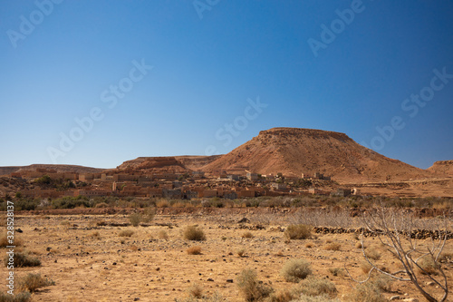 Old village hidden on the desert valley between hills on blue sky background