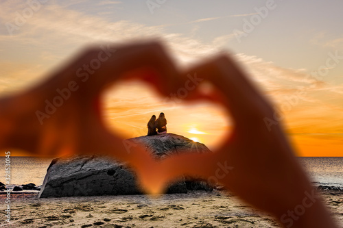 Hand in Herzform vor einem Liebespaar am Strand