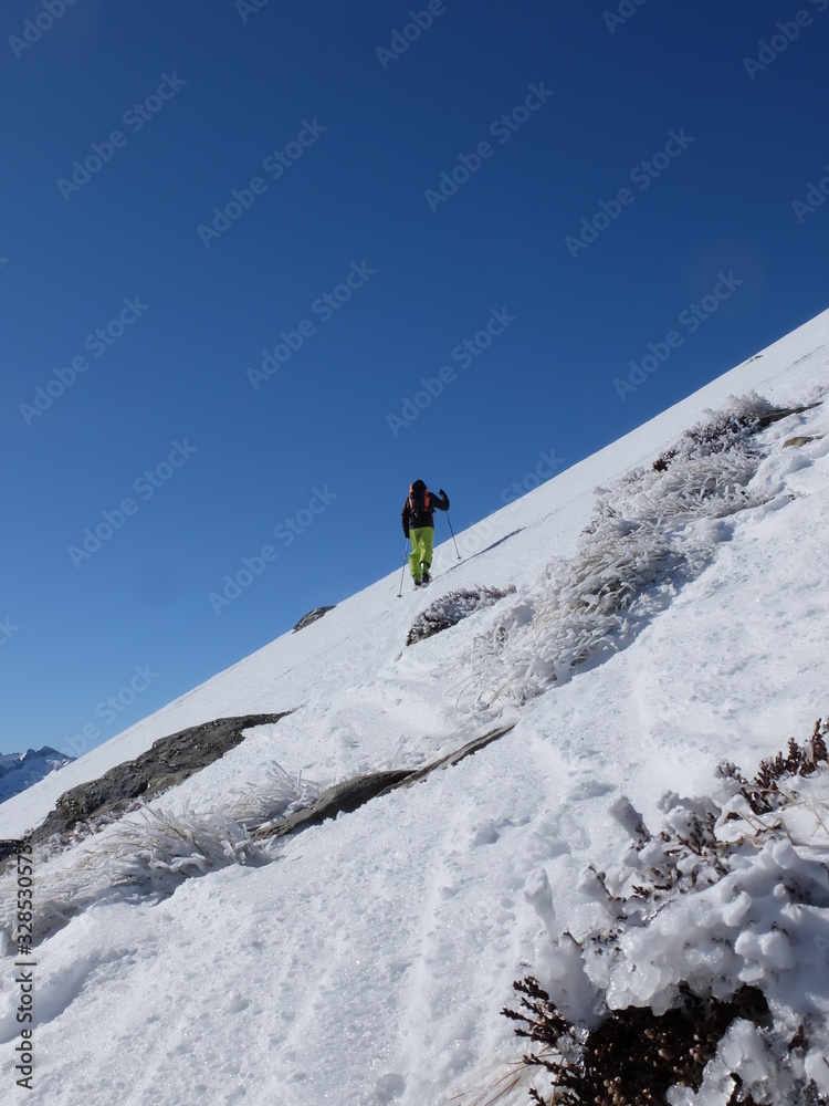 Alpiniste qui grimpe dans la neige et la glace de la montagne avec des bâtons et des crampons sous le ciel grand bleu