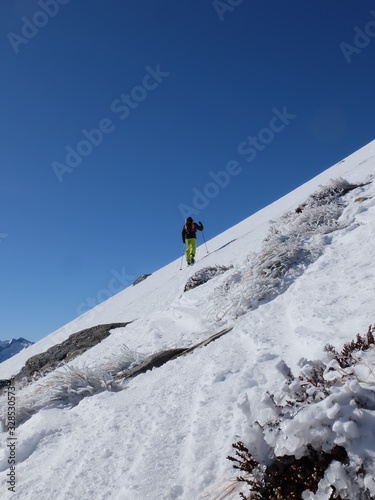 Alpiniste qui grimpe dans la neige et la glace de la montagne avec des bâtons et des crampons sous le ciel grand bleu © Ourson+