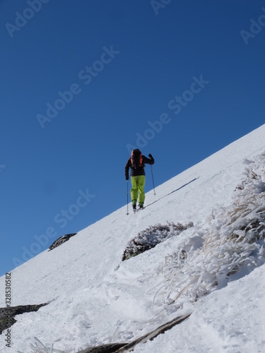 Alpiniste qui grimpe dans la neige et la glace de la montagne avec des bâtons et des crampons sous le ciel grand bleu