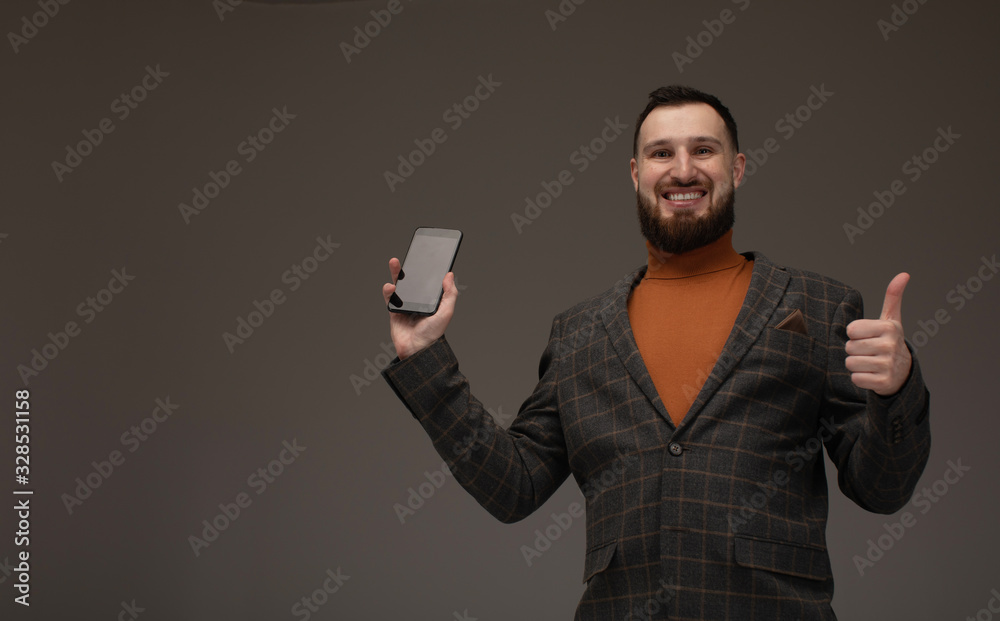Handsome bearded model is posing with phone in hands over grey background. Handsome bearded model is posing with phone in hands over grey background.