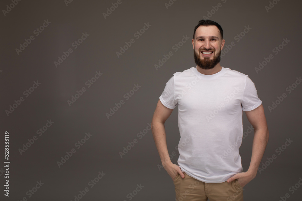 Handsome young bearded man on grey background looking at camera. Portrait of laughing young man. Handsome young bearded man on grey background looking at camera. Portrait of laughing young man.