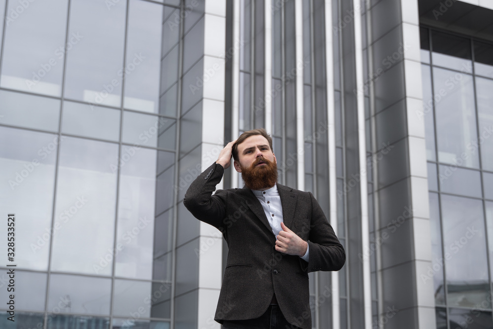Portrait of an handsome businessman wearing jacket over office building in financial district outdoors. Young bearded Businessman outdoor. Successful entrepreneur dressed in formal wear. Portrait of an handsome businessman wearing jacket over office building in financial district outdoors. Young bearded Businessman outdoor. Successful entrepreneur dressed in formal wear.