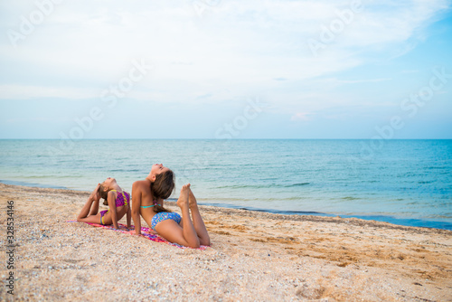 Charming little girls do gymnastic exercises on sea sand
