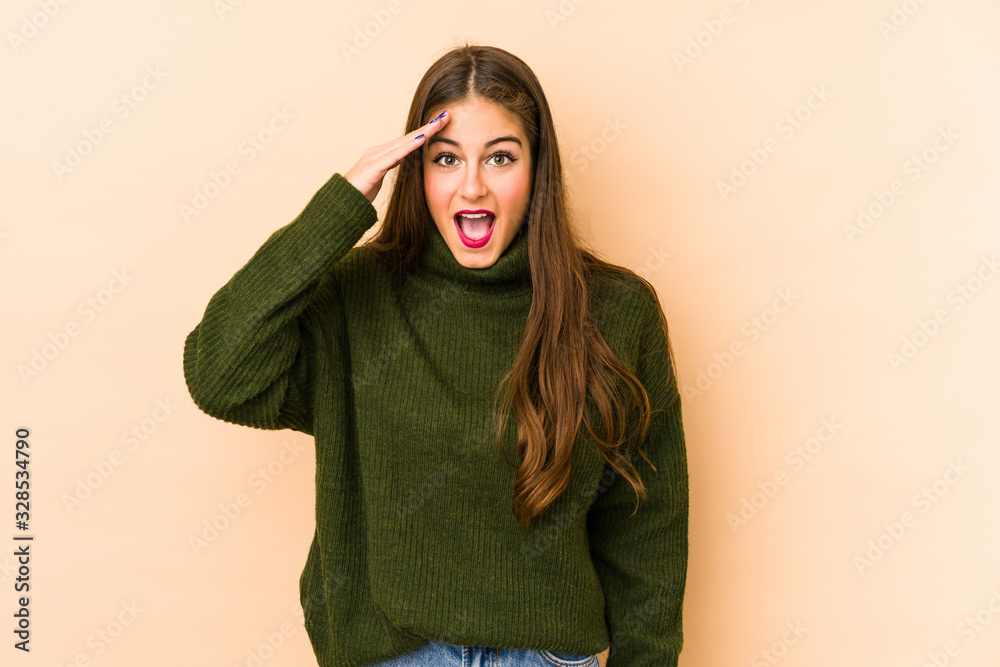 Young caucasian woman isolated en beige background shouts loud, keeps eyes opened and hands tense. Young caucasian woman isolated en beige background shouts loud, keeps eyes opened and hands tense.