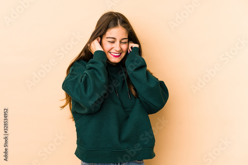Young caucasian woman isolated en beige background covering ears with hands. © Asier