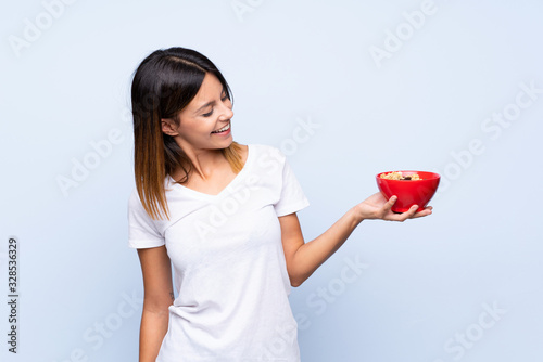 Young woman over isolated blue background holding a bowl of cereals