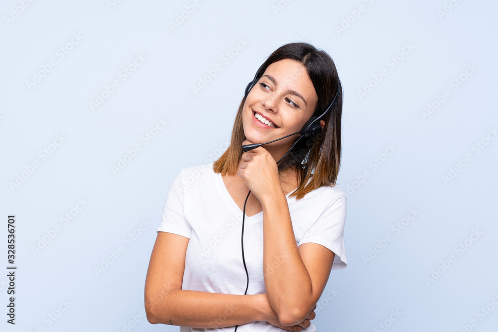 Young woman over isolated blue background working with headset looking side Young woman over isolated blue background working with headset looking side