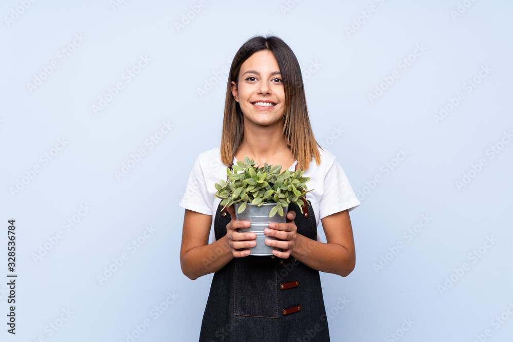 Young woman over isolated blue background taking a flowerpot Young woman over isolated blue background taking a flowerpot