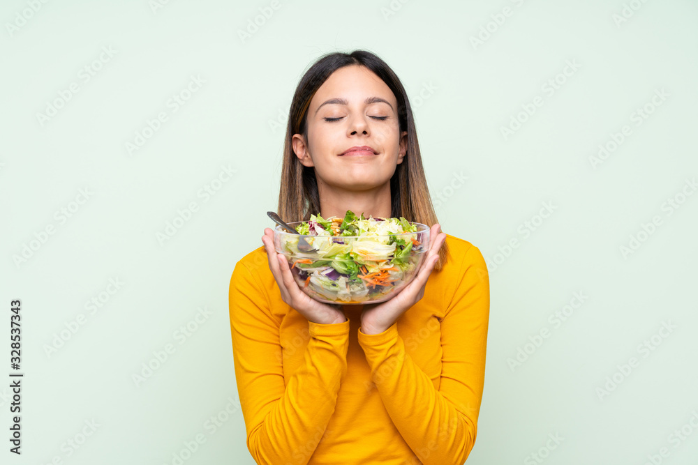 Young woman with salad over isolated green wall Young woman with salad over isolated green wall