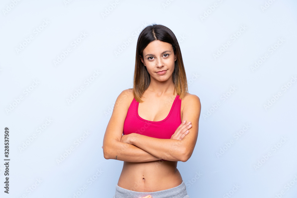 Young sport woman over isolated blue background with arms crossed