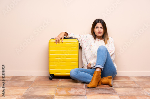 Traveler woman with suitcase sitting on the floor having doubts and with confuse face expression photo