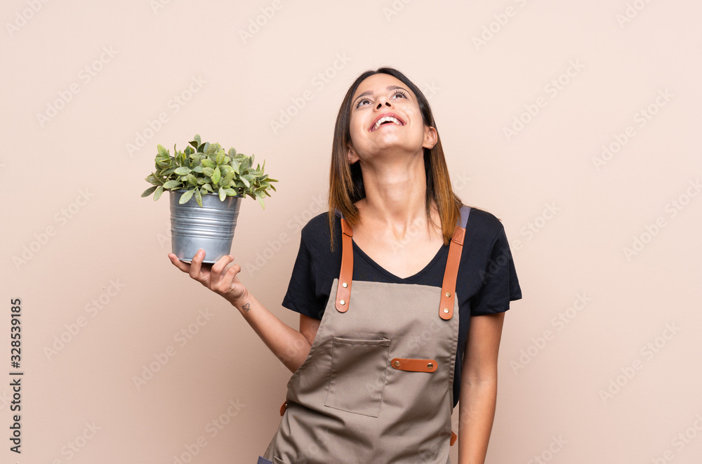 Young woman holding a plant looking up while smiling Young woman holding a plant looking up while smiling