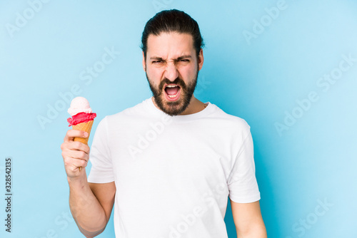 Young caucasian man eating an ice cream isolated screaming very angry and aggressive.