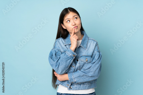 Fotografie Young asian woman isolated on background having doubts while looking up