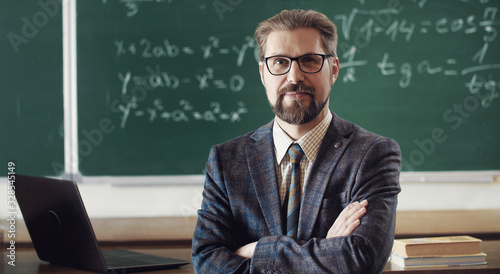 Fotografia Portrait of smiling mature teacher in classic suit and eyewear standing cross-ar