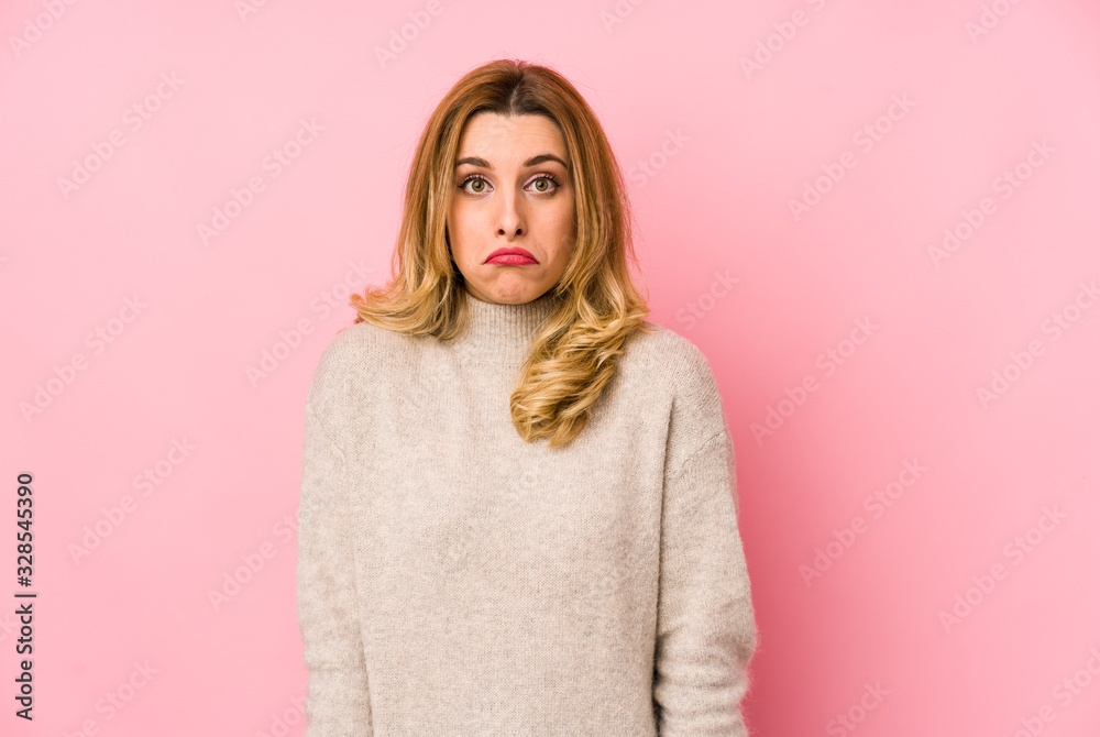 Young blonde cute woman wearing a sweater isolated shrugs shoulders and open eyes confused. Young blonde cute woman wearing a sweater isolated shrugs shoulders and open eyes confused.