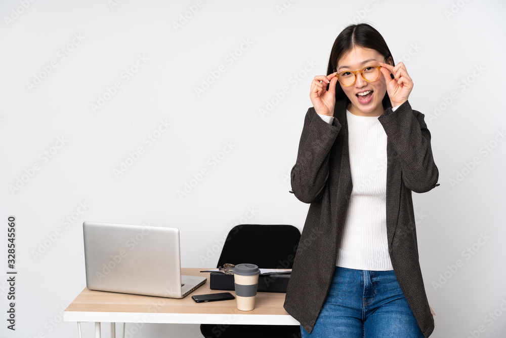 Business asian woman in her workplace isolated on white background with glasses and surprised