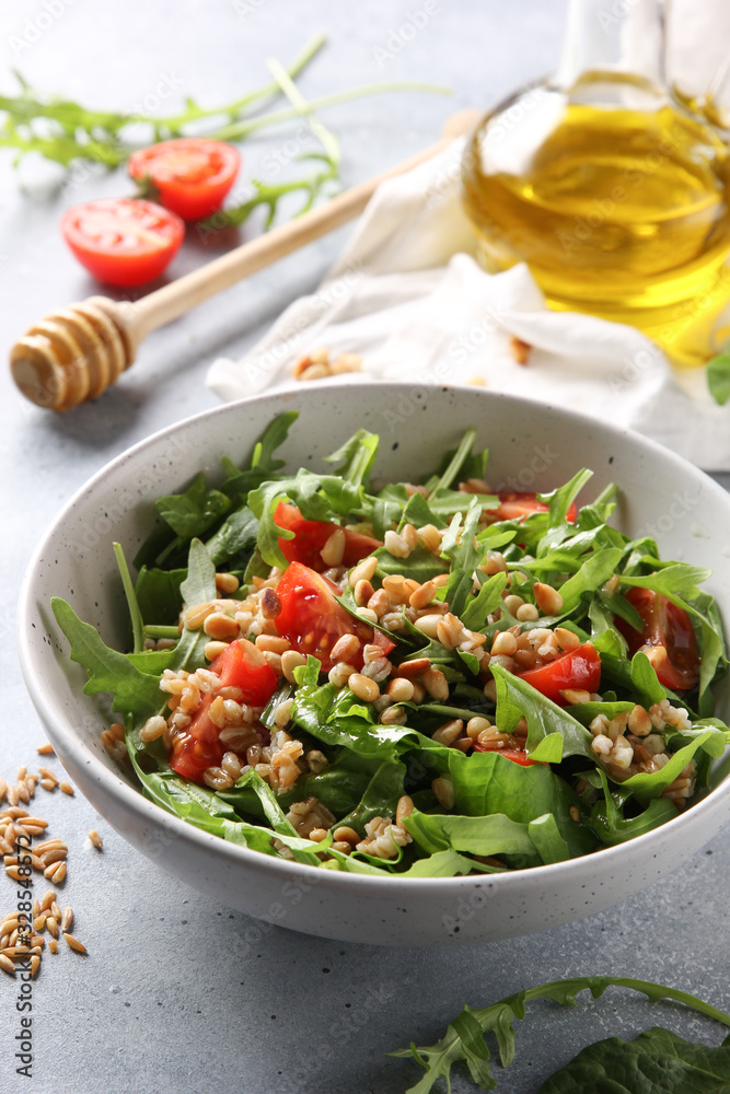 The concept of healthy food. Leaf salad with grits and pine nuts in a deep bowl. Arugula, spinach, tomatoes, spelt, olive oil, honey on a light background. Background image, copy space The concept of healthy food. Leaf salad with grits and pine nuts in a deep bowl. Arugula, spinach, tomatoes, spelt, olive oil, honey on a light background. Background image, copy space