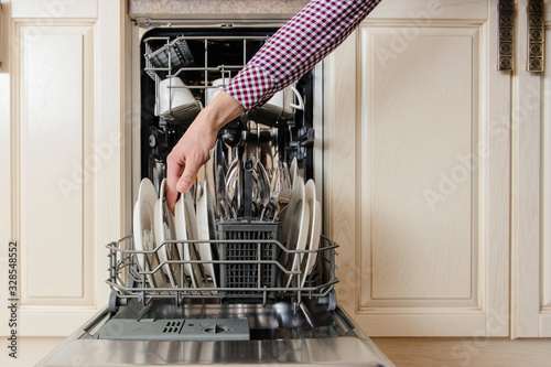 Close up man hand hold plate in open dishwasher photo