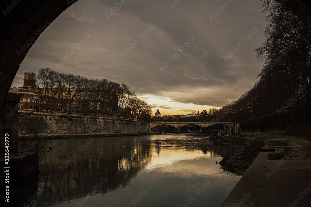Cityscape and panoramic view of old bridge with warm sunset sky  reflections in water of Tiber river and dome of St. Peters cathedral church with old buildings and architecture in Rome, Italy.