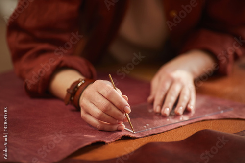 Horizontal close up shot of beautiful female artisan's hands cutting out leather material