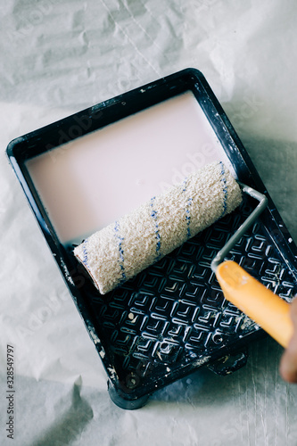 the roller is wetted in a liquid primer in a plastic black container, before painting the walls with paint photo