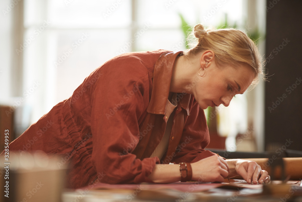 Horizontal medium side view portrait of beautiful Caucasian woman with blond hair working in her leather craft workshop Horizontal medium side view portrait of beautiful Caucasian woman with blond hair working in her leather craft workshop
