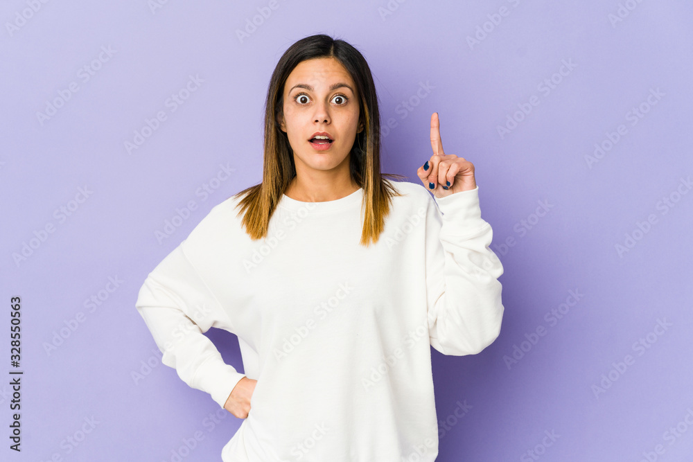 Young woman isolated on purple background pointing upside with opened mouth.