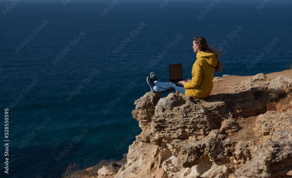 A freelancer girl is working typing on a laptop and looking at a monitor with a beautiful view of the open air sea sky. Traveling with a computer. Online dream job. A freelancer girl is working typing on a laptop and looking at a monitor with a beautiful view of the open air sea sky. Traveling with a computer. Online dream job.